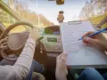 Egzamin na prawo jazdy w toku. Kandydat trzyma kierownicę, a egzaminator zaznacza na liście kontrolnej, czy spełnione są wszystkie kategorie prawa jazdy.