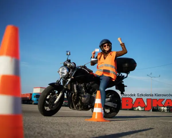 Szczęśliwa kursantka z prawem jazdy kat. A na motocyklu, w kamizelce odblaskowej, na placu manewrowym.