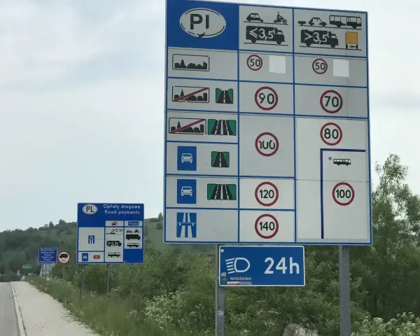 Znaki drogowe informujące o opłatach i limitach prędkości na drodze dwujezdniowej.