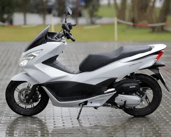 Biały skuter Honda PCX na mokrym bruku. Zastanawiasz się, od ilu lat można jeździć skuterem 50? Od 14 roku życia z kartą motorowerową.